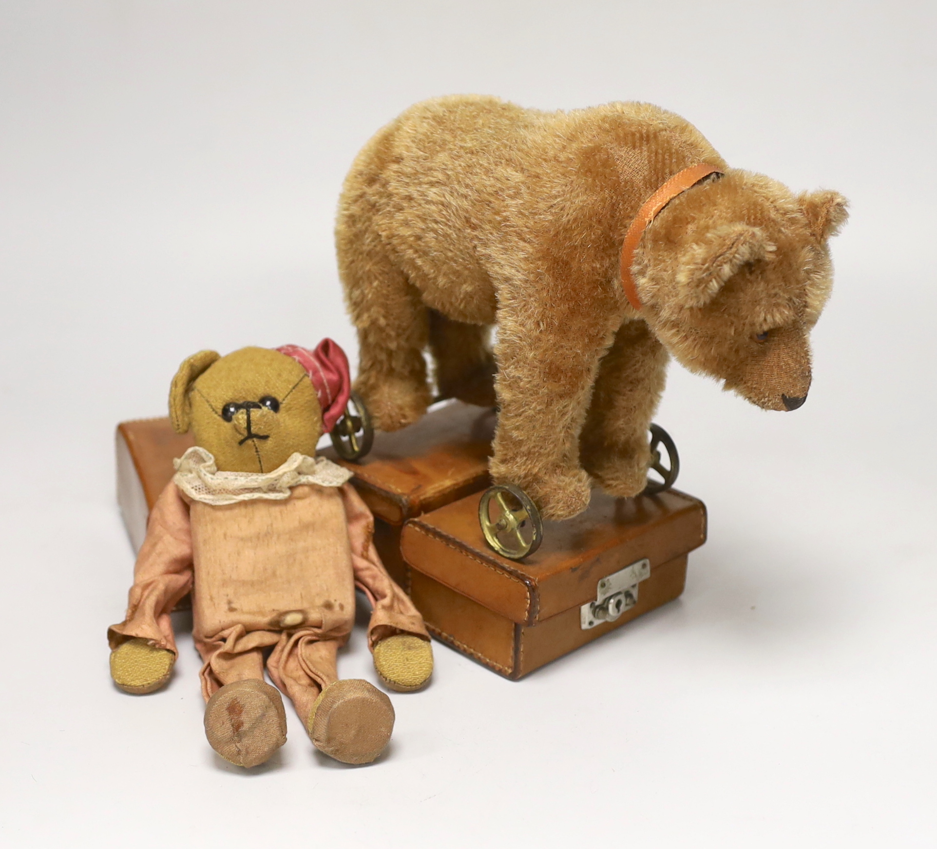 A Steiff bear on wheels, glass eyes, with original collar, no button, c.1920, height to shoulder 7in., good condition with slight thinning to mohair left shoulder, and a dressed mechanical bear, c.1920's, 8in., inoperati